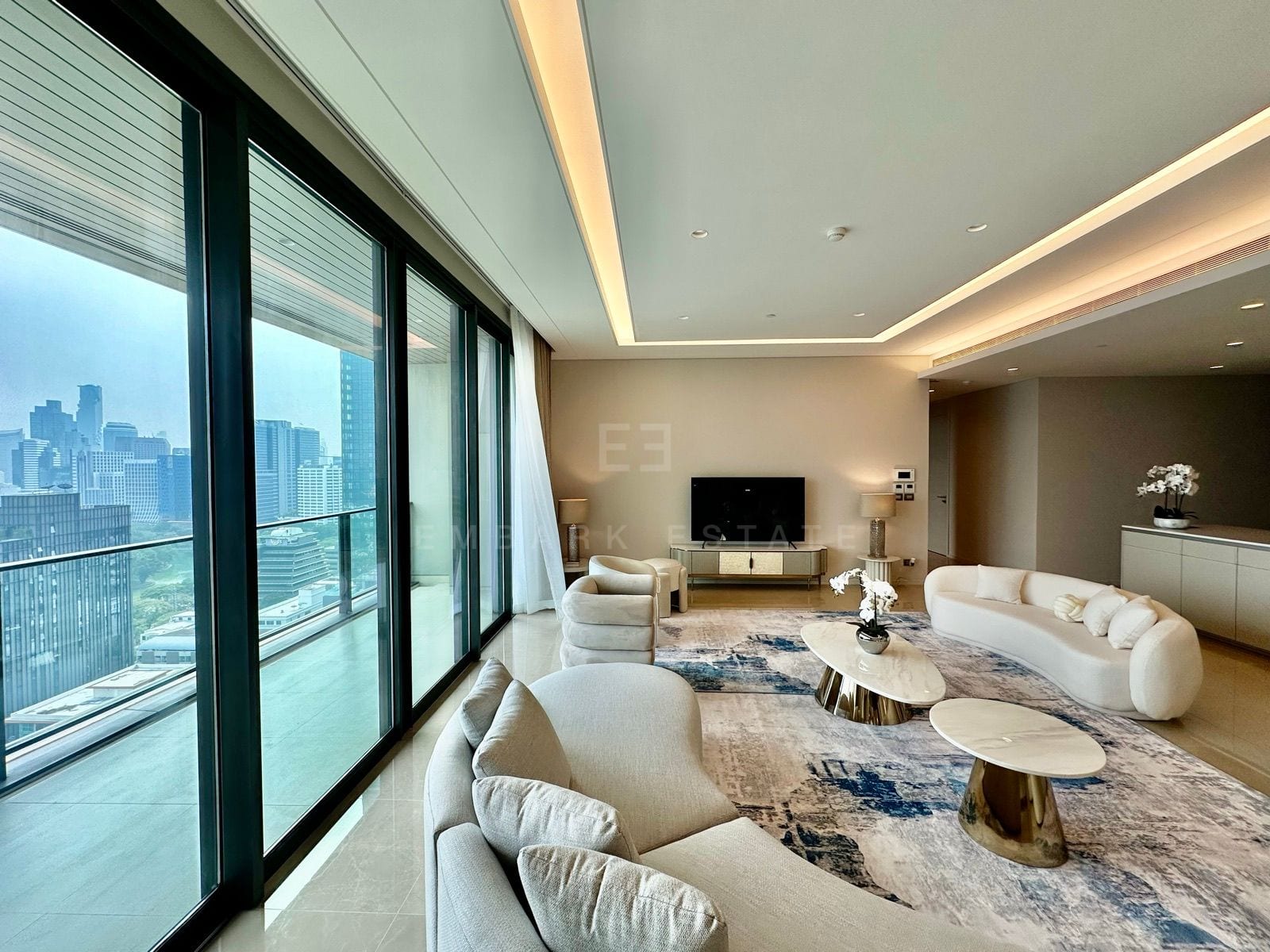 The living room of the 5-bedroom residence at the Residences at Sindhorn Kempinski, Bangkok, with curved cream sofas and windows over the central Bangkok skyline