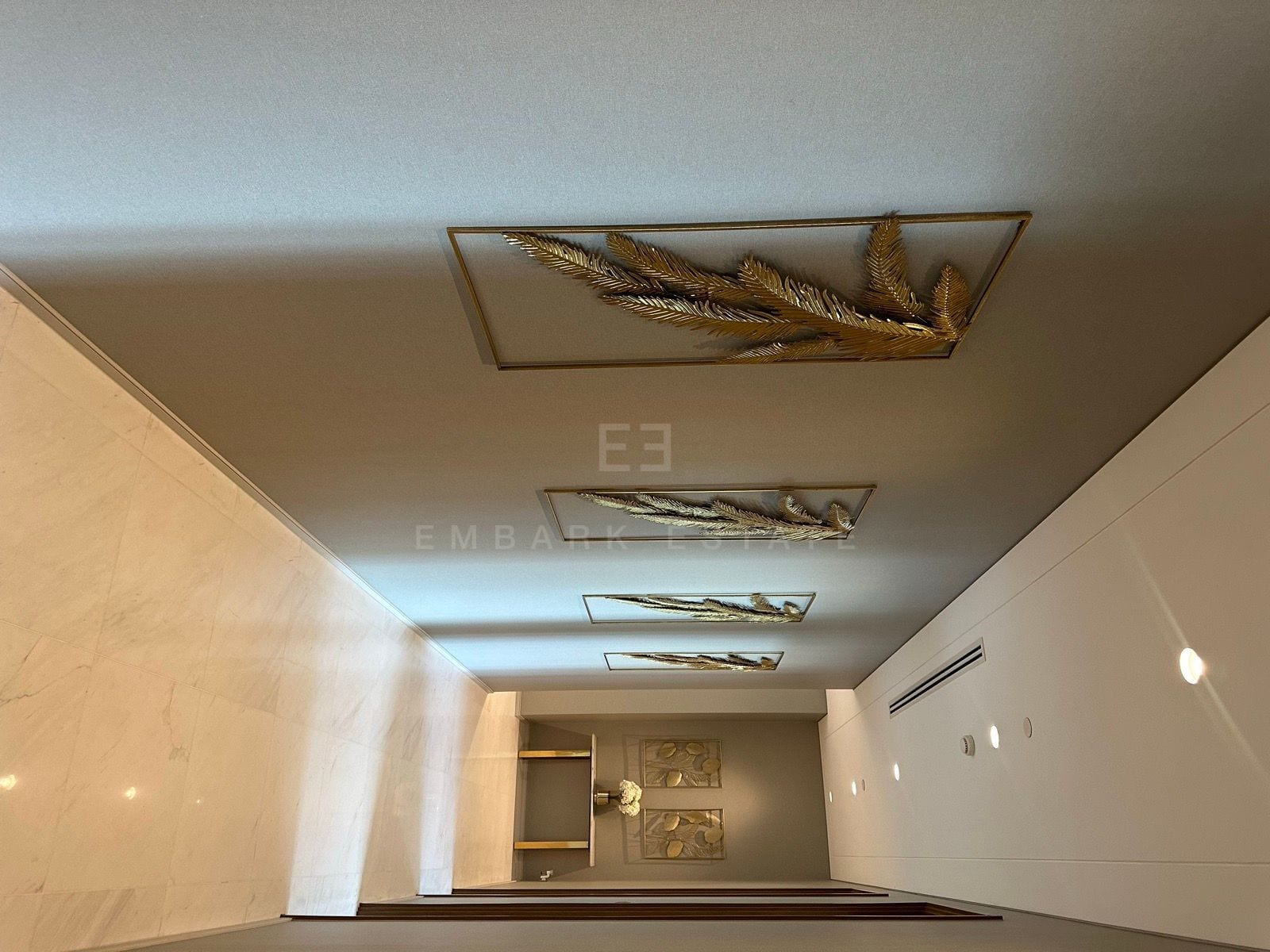 A hallway in the junior penthouse at the Residences at Sindhorn Kempinski, Bangkok, lined with framed gold palm-leaf panels above a marble floor