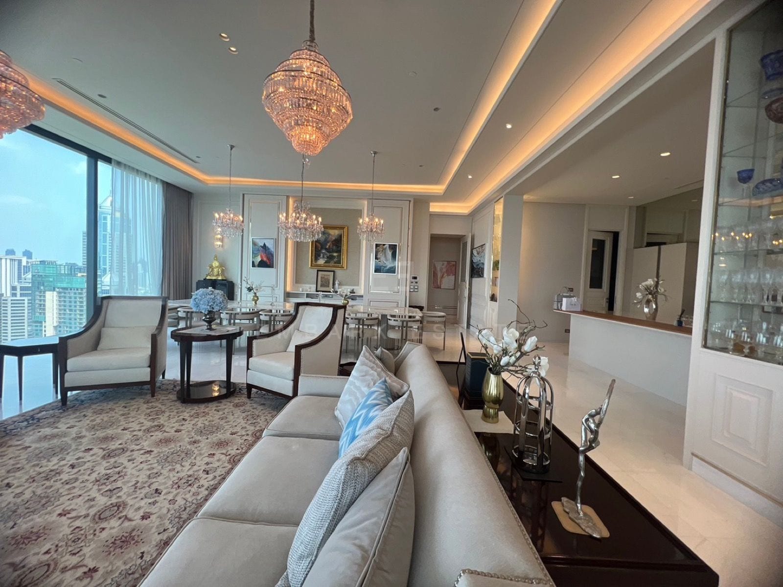 ห้องนั่งเล่นและห้องอาหารของแกรนด์เพนต์เฮาส์ที่ The Residences at Sindhorn Kempinski Hotel Bangkok พร้อมโคมระย้าคริสตัลและวิวเมือง