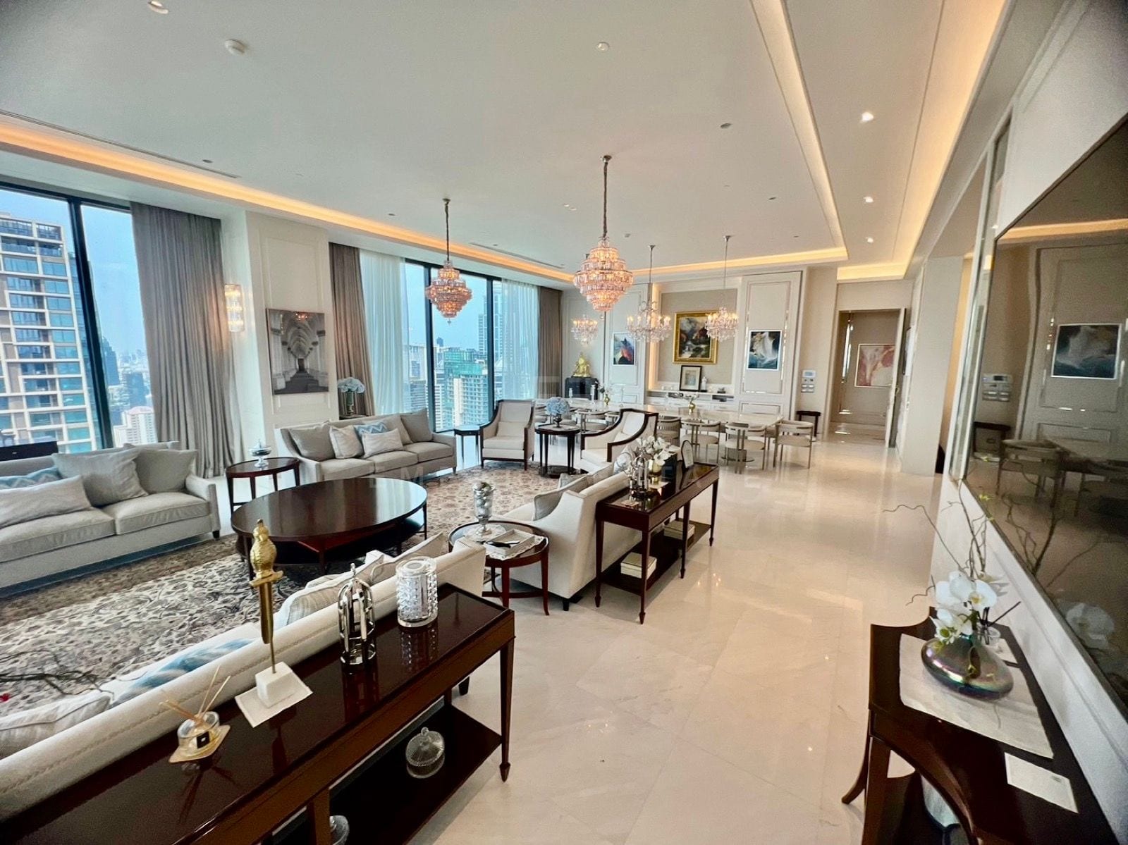 ห้องนั่งเล่นของแกรนด์เพนต์เฮาส์ที่ The Residences at Sindhorn Kempinski Hotel Bangkok พร้อมโซฟา โคมระย้า และหน้าต่างมองเห็นตัวเมือง