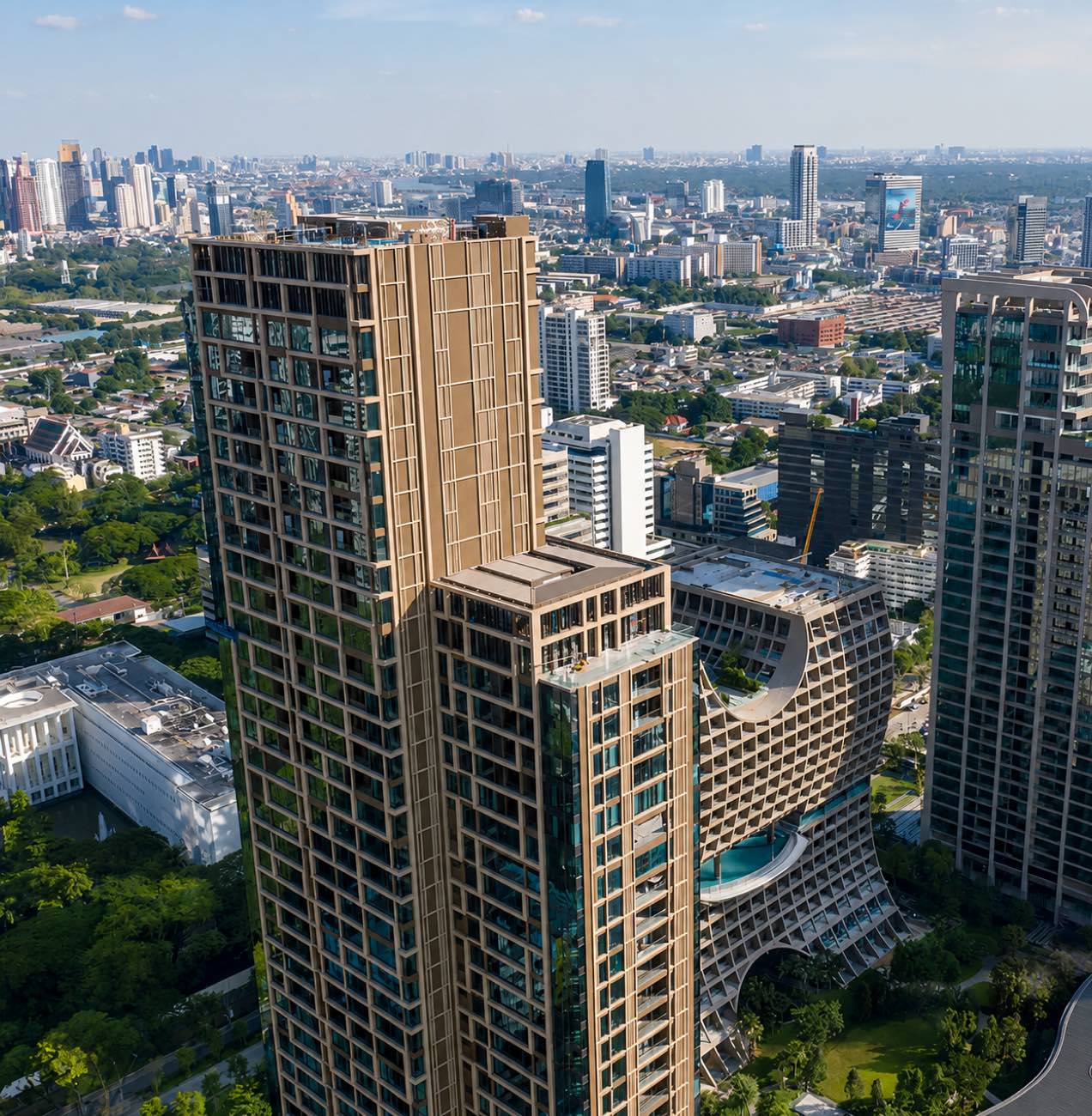 Sindhorn Residence Langsuan: the gold-finned residential tower seen from the air above the greenery of central Bangkok, by Siam Sindhorn