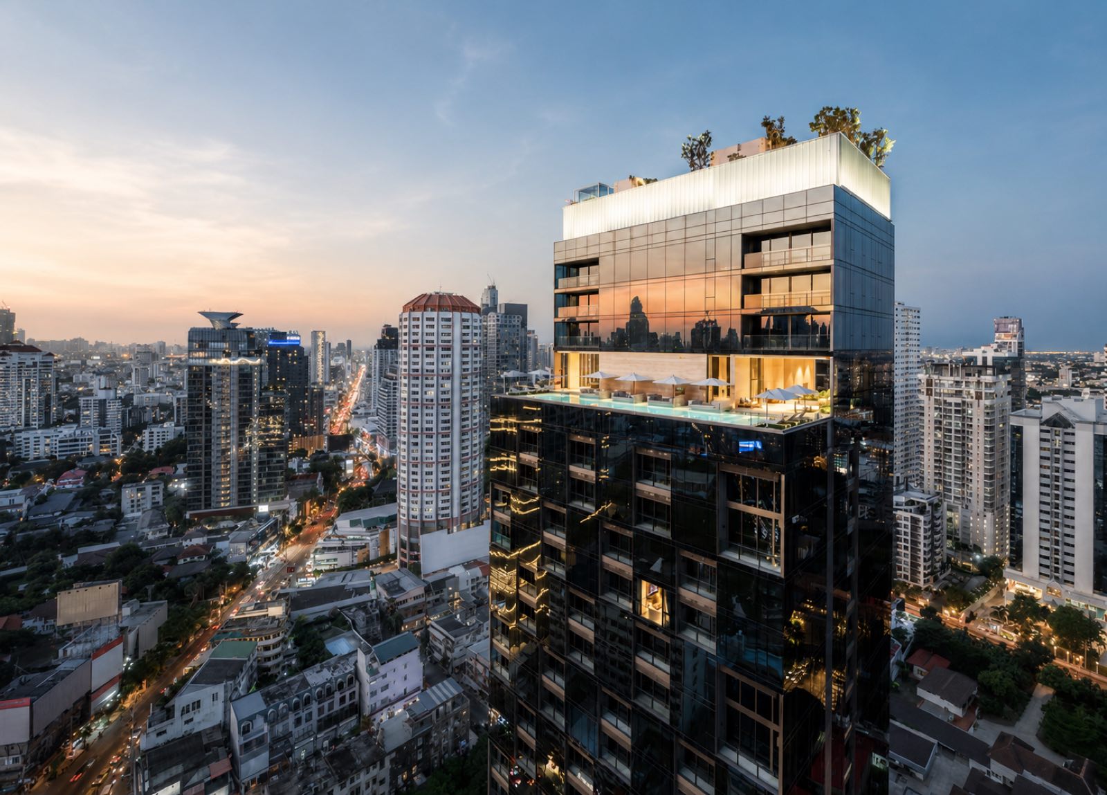 The Strand Thonglor: the tower crown with its rooftop infinity pool and sky garden lit at dusk above the Thonglor skyline in central Bangkok