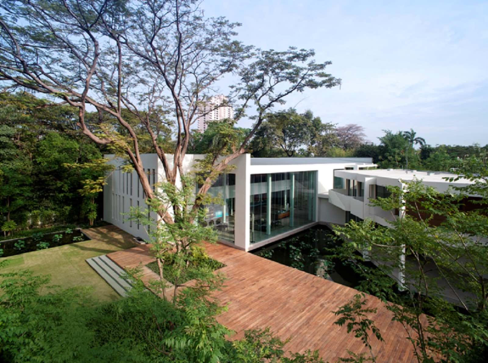 The Sukhothai Residences: Glass-walled clubhouse pavilion set among mature trees with a timber deck over water
