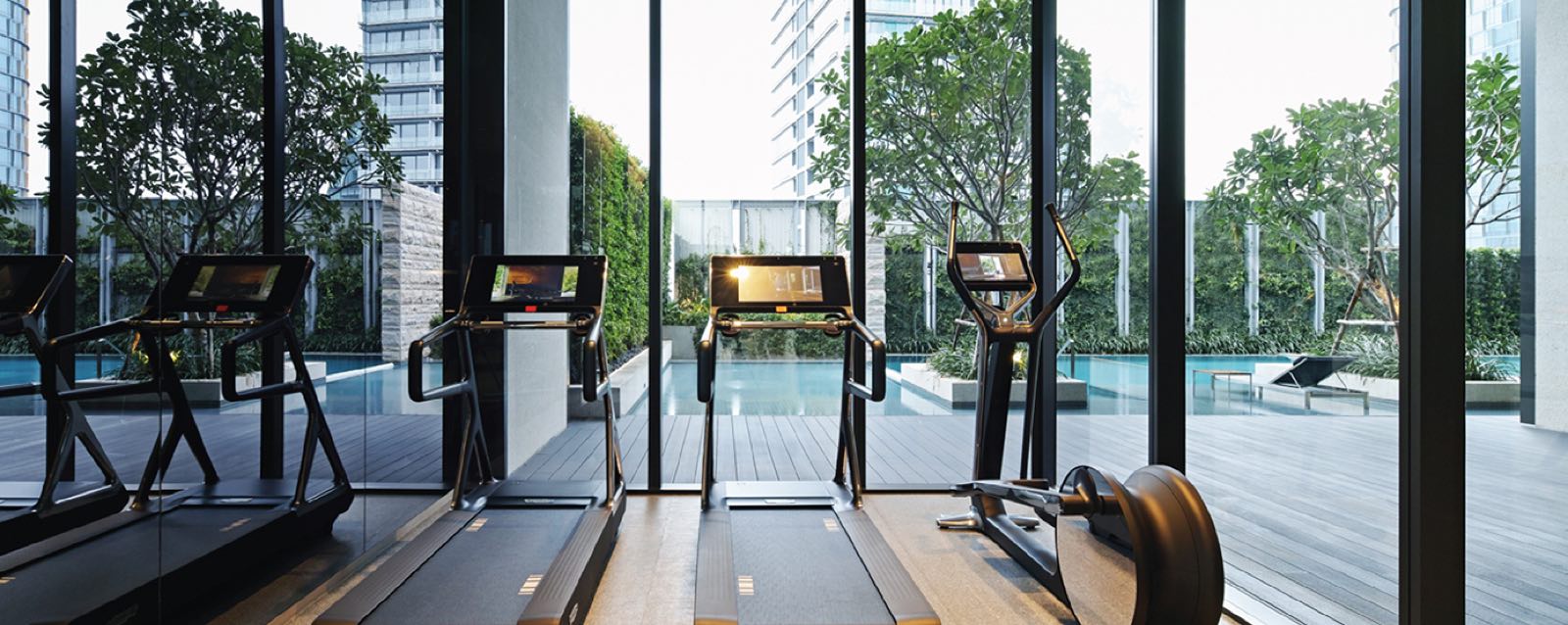 TELA Thonglor: Fitness gym with treadmills and cardio equipment overlooking the pool and green wall through glass