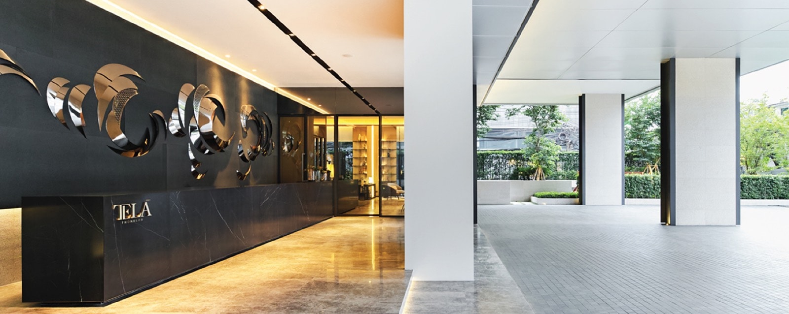 TELA Thonglor: main lobby and reception with sculptural metallic wall art and a black marble desk carrying the TELA name