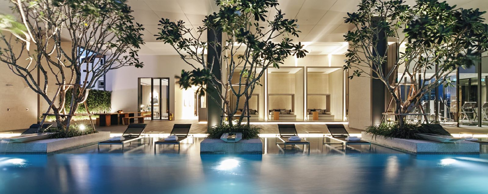 TELA Thonglor: Swimming pool and garden cabana deck at dusk, framed by frangipani trees and sun loungers