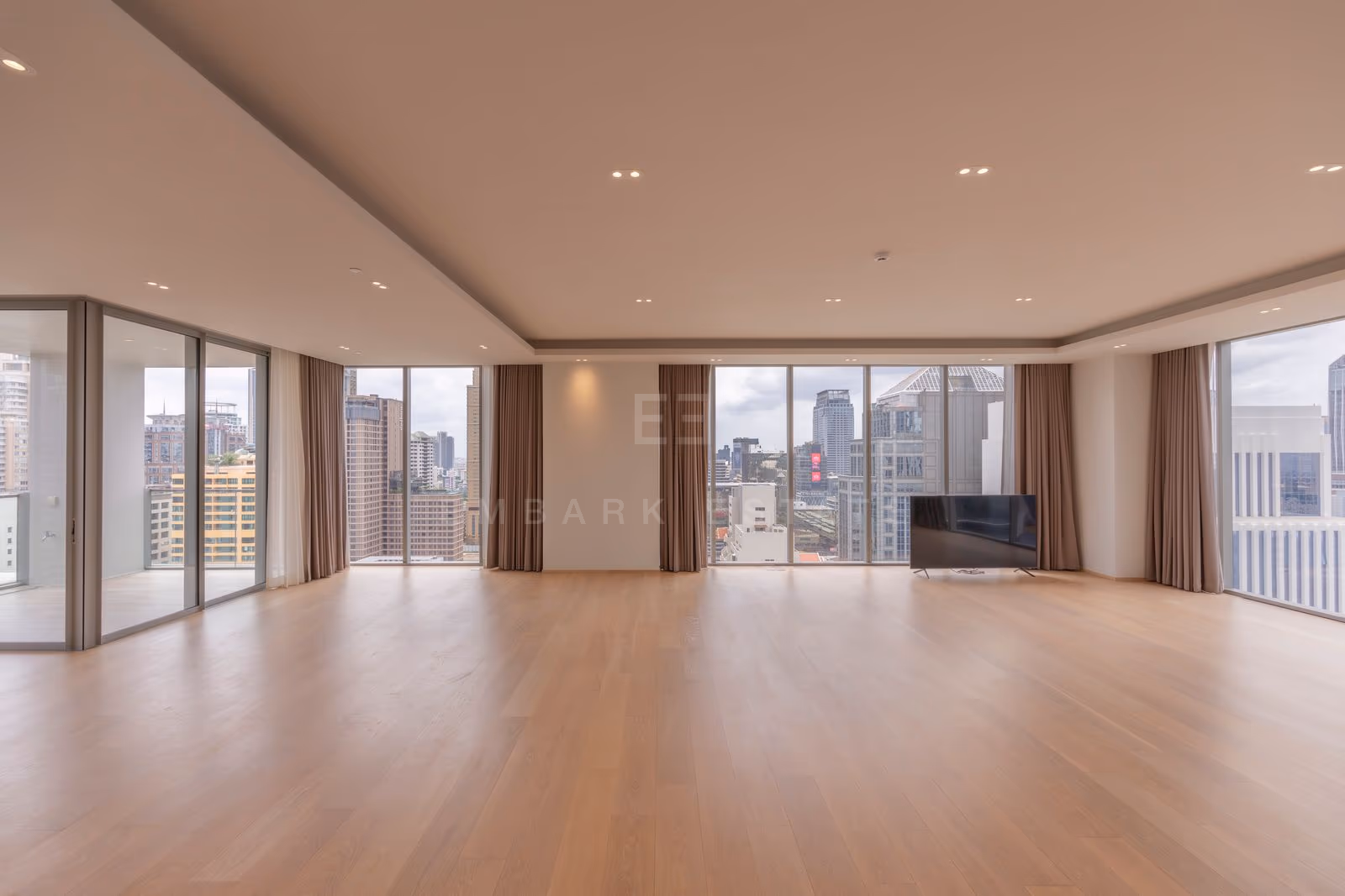The living room of a three-bedroom residence at Tonson One Residence, 24th floor, unfurnished, pale oak floors and full-height glazing on two sides over central Bangkok