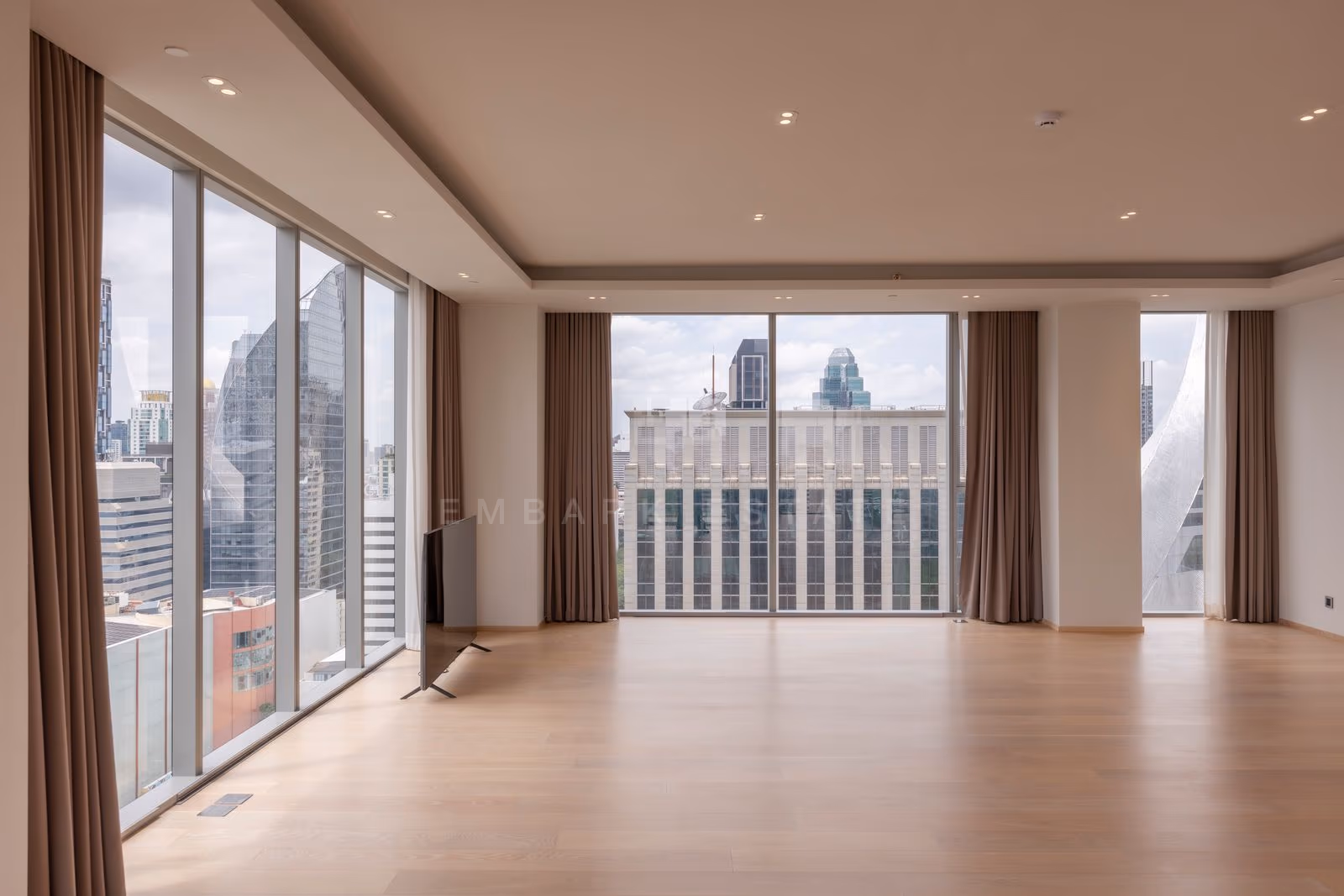 The corner glazing of the living room in a three-bedroom residence at Tonson One Residence, curtains drawn back, the city on both sides