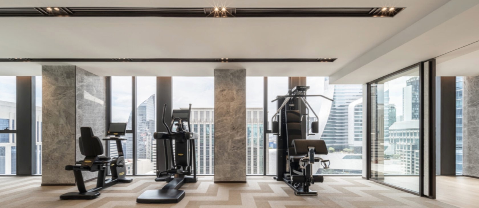 The fitness centre with Technogym equipment and floor-to-ceiling skyline views at Tonson One, central Bangkok