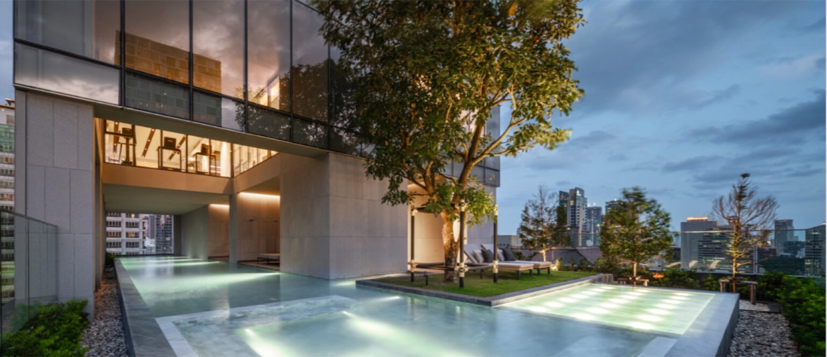 The rooftop infinity pool and lit garden deck at Tonson One at dusk in central Bangkok