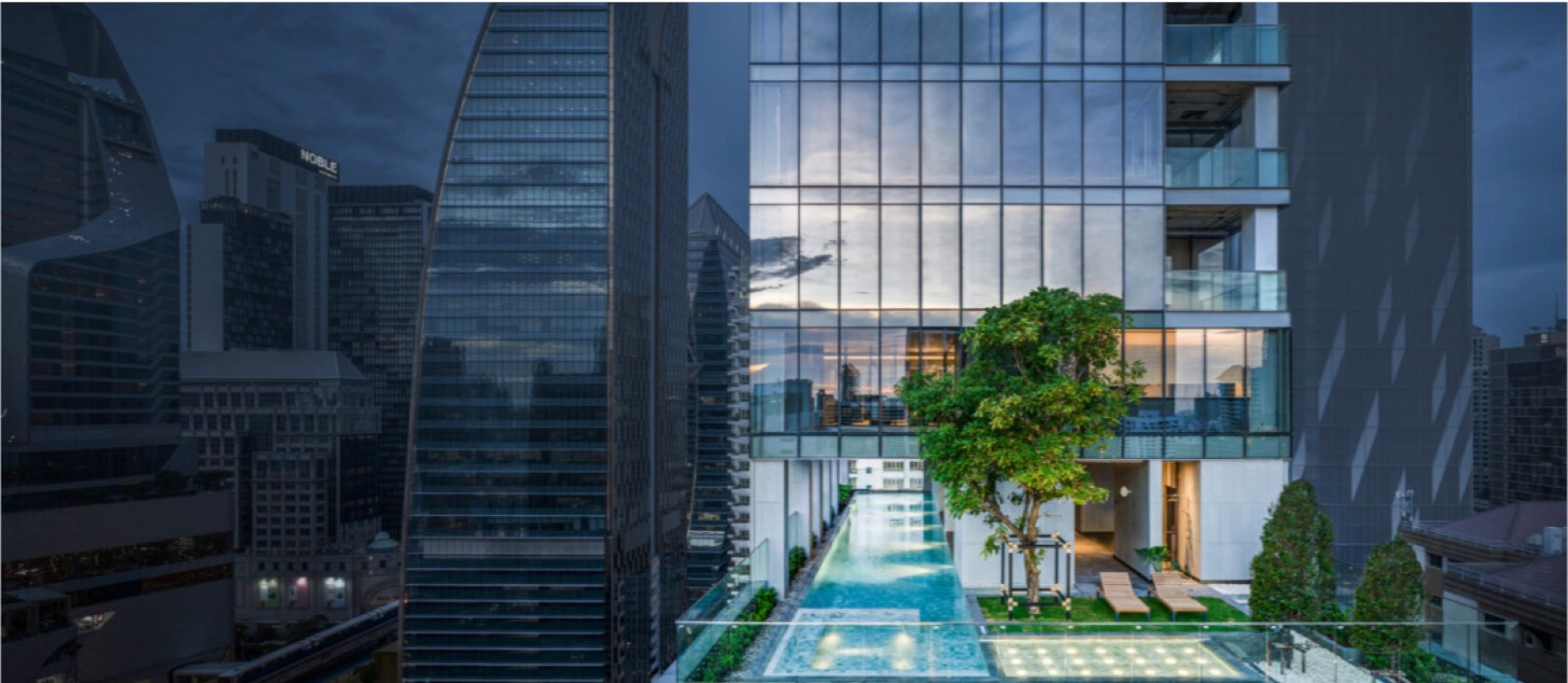 The cantilevered glass-edged sky pool and garden terrace at Tonson One at dusk above the Bangkok skyline