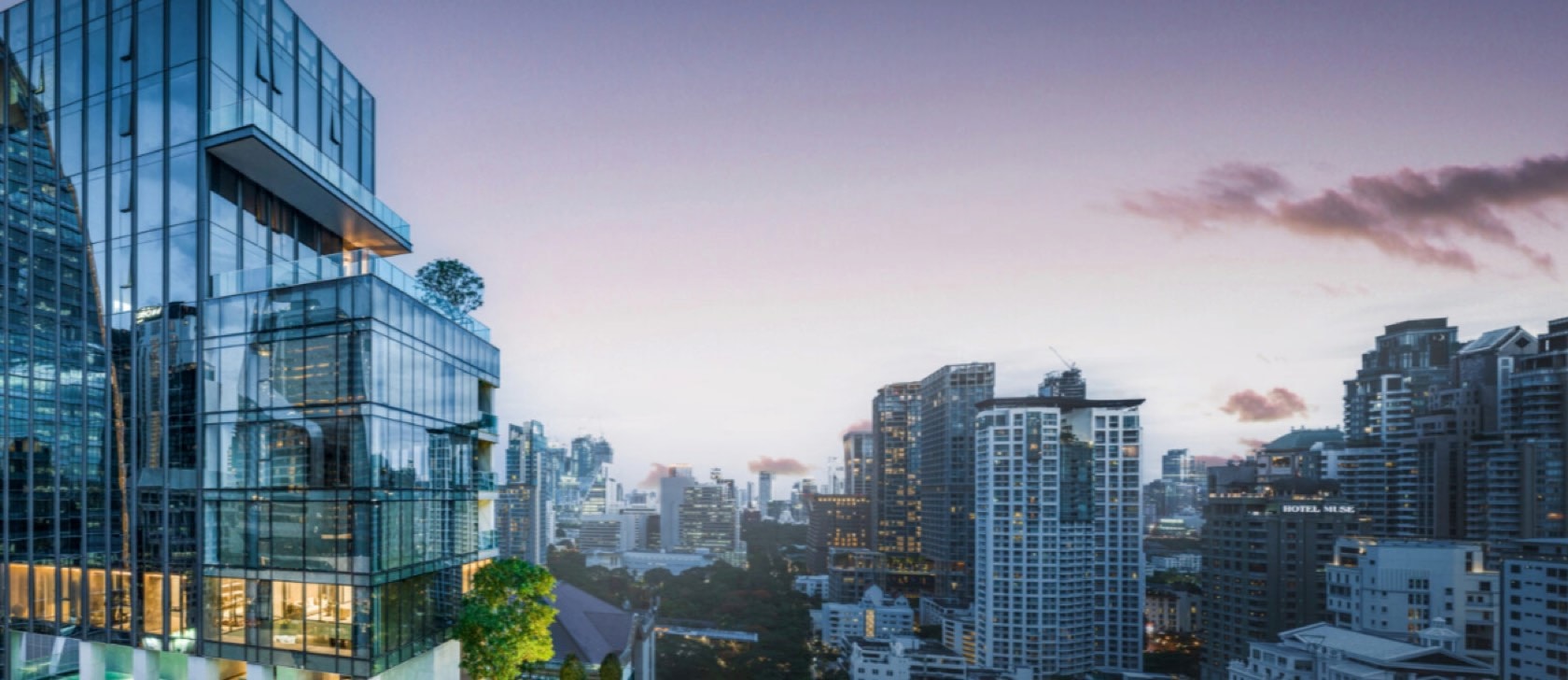 The upper floors and glass crown of Tonson One at dusk above the central Bangkok skyline