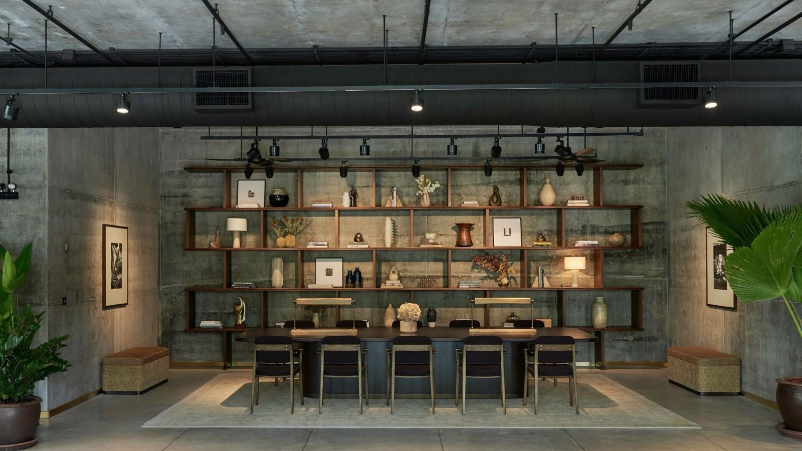 Windshell Naradhiwas residents' lounge with a library wall and communal dining table, exposed concrete ceiling