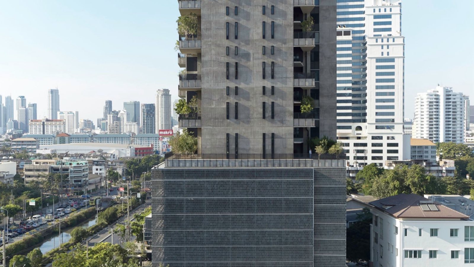 Windshell Naradhiwas tower facade detail, perforated concrete screen and cantilevered balconies against the Bangkok skyline