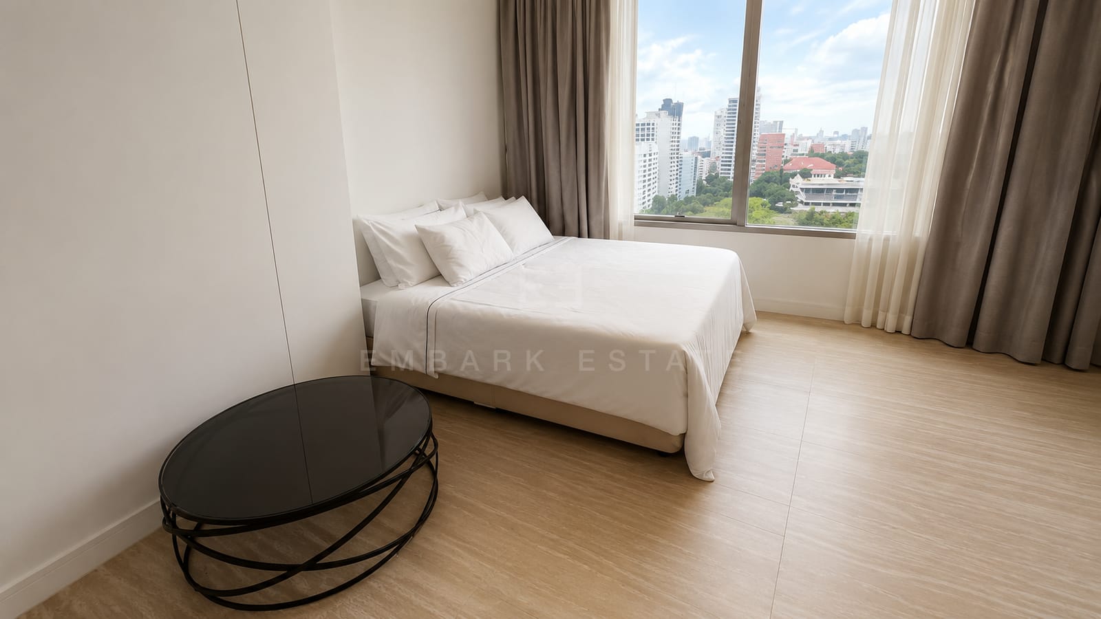 A bedroom at 185 Rajadamri, white linen with a black oval table beside the curtained window