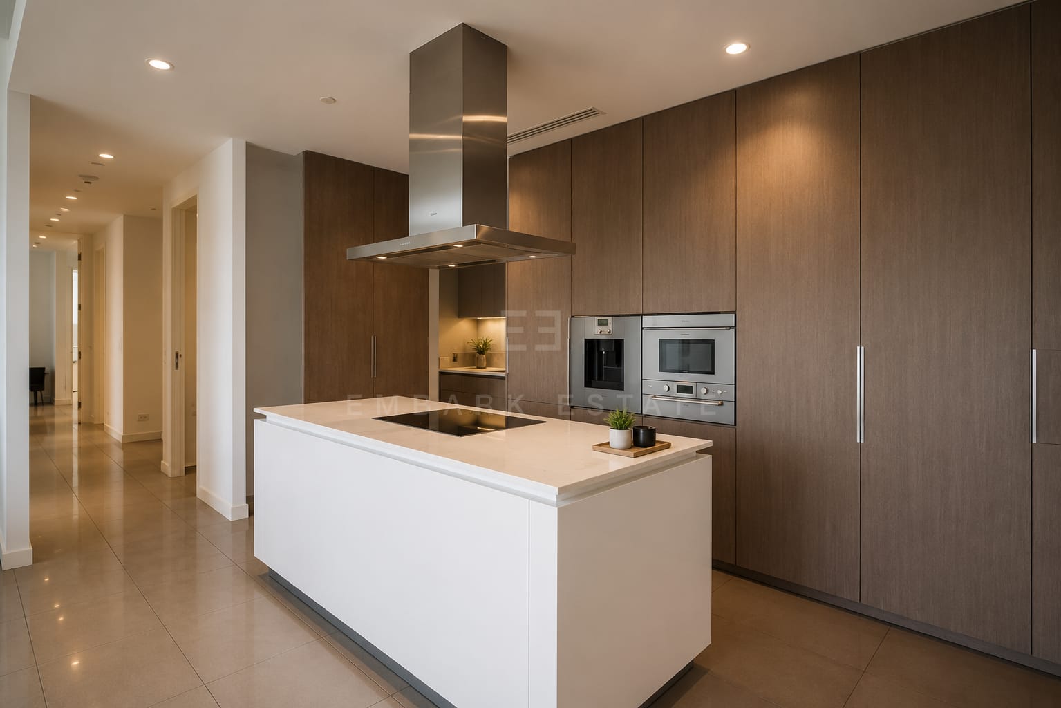The kitchen at 185 Rajadamri, a white island with an induction hob and extractor against full-height walnut joinery