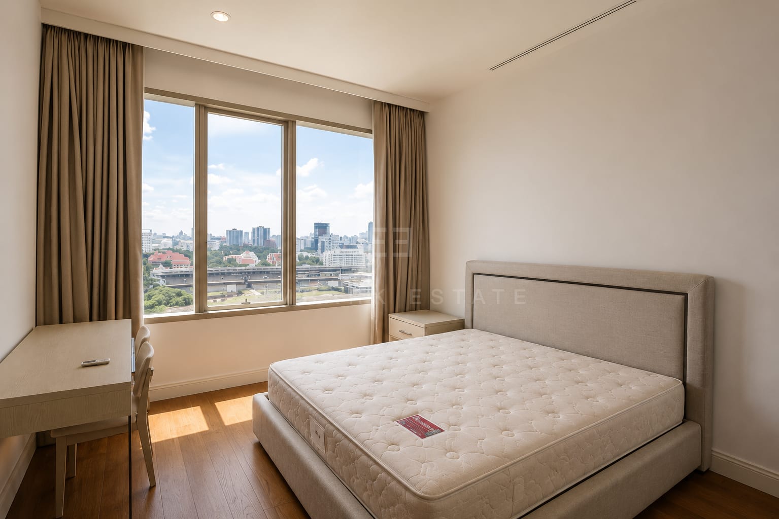 A bedroom at 185 Rajadamri, a taupe upholstered headboard with a desk at the window over the city