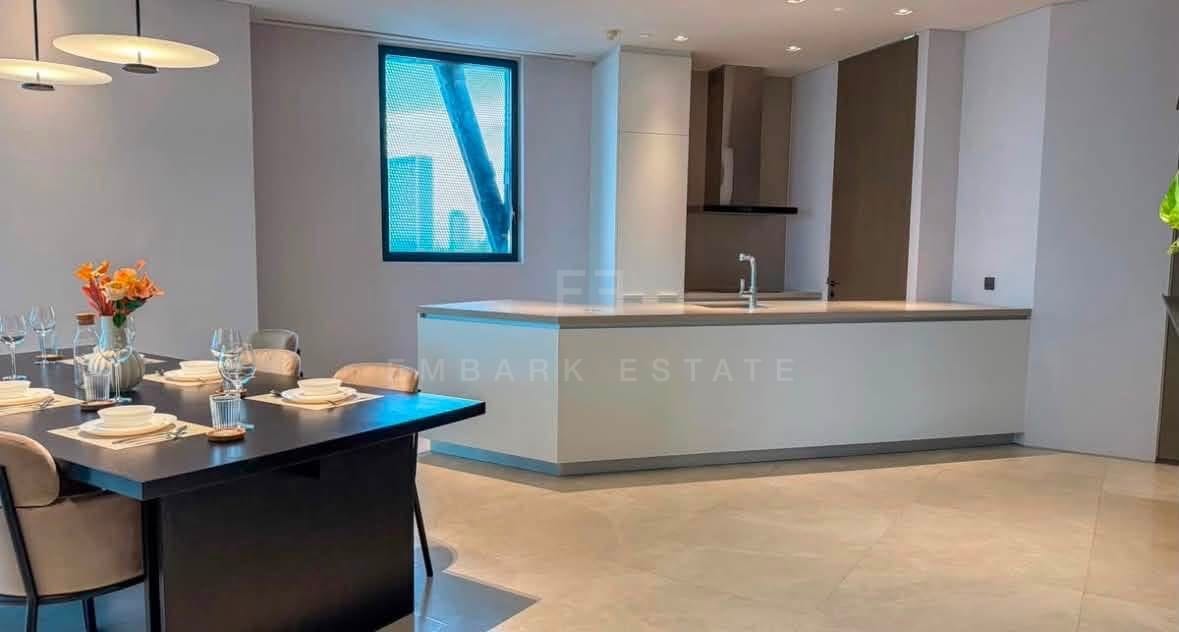 The kitchen at Banyan Tree Residences Riverside, a long island in pale stone with the dining table in the foreground and fitted timber cabinetry behind