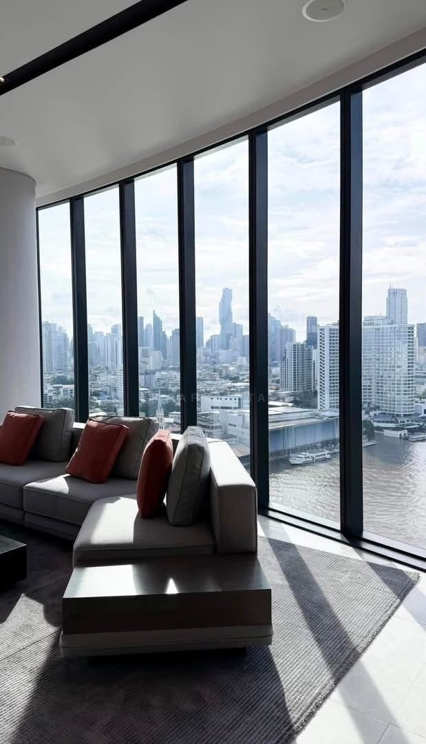 The corner glazing at Banyan Tree Residences Riverside, a grey sofa facing the Chao Phraya with the Silom and Sathorn towers on the far bank