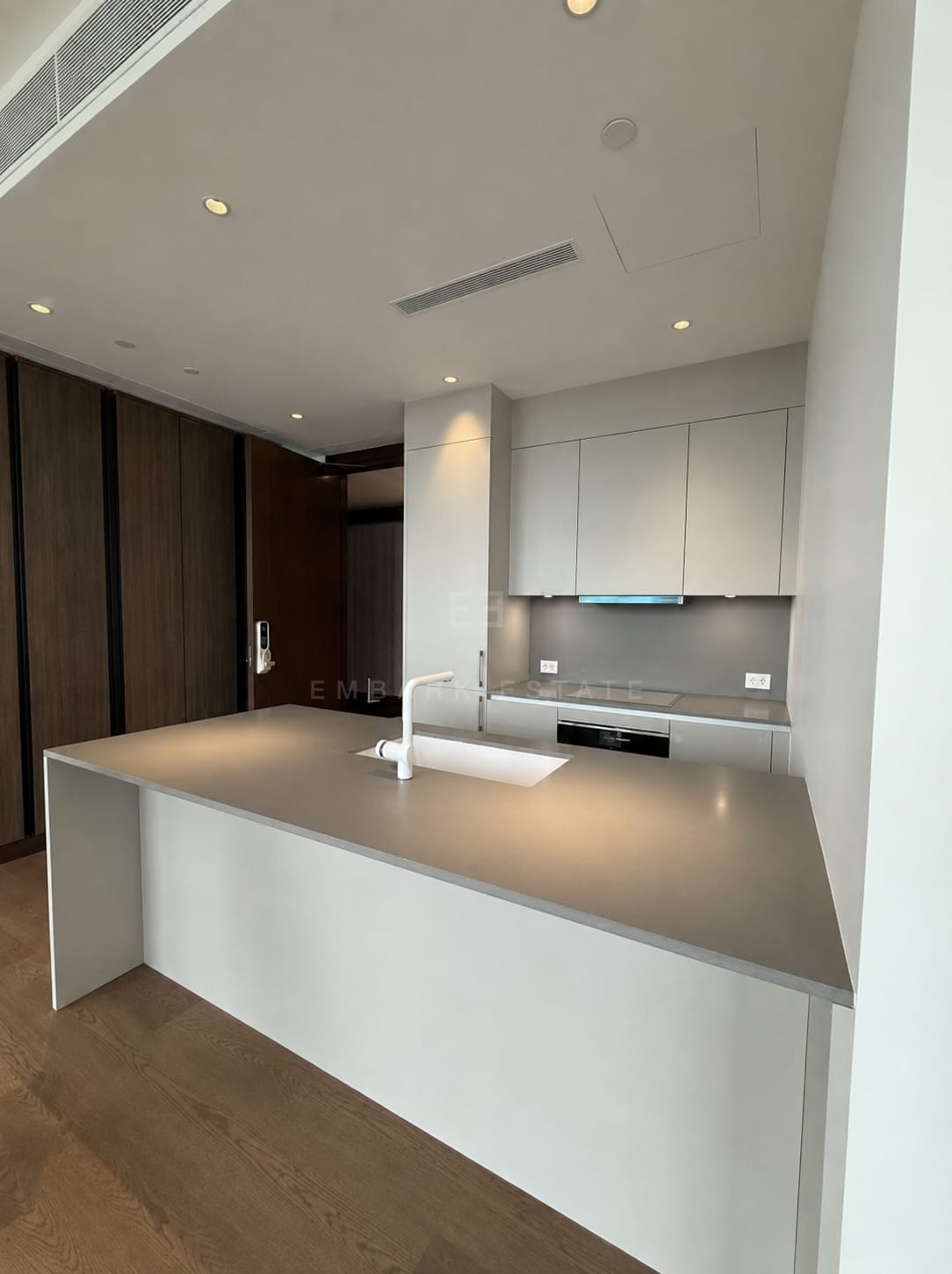 The kitchen of the 110 square metre residence at Dusit Parkside, Dusit Central Park, a long island with an inset sink against a dark timber joinery wall