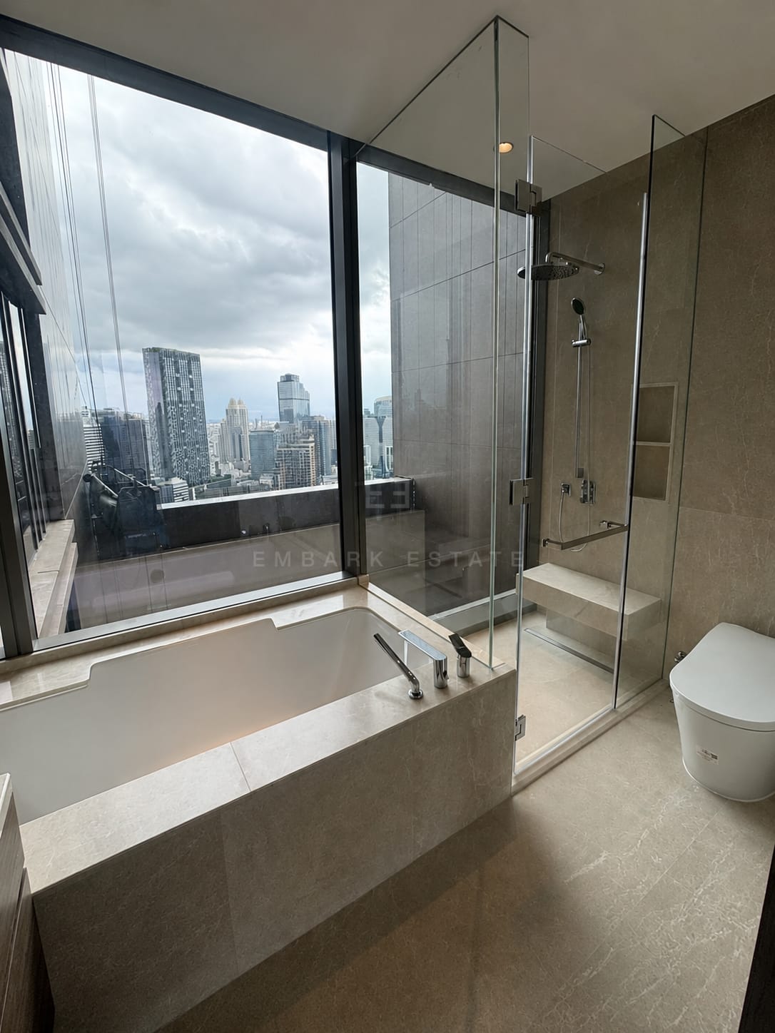 Master bathroom at Dusit Residences, Dusit Central Park, Bangkok, with a stone-set bathtub and walk-in shower beside a city window