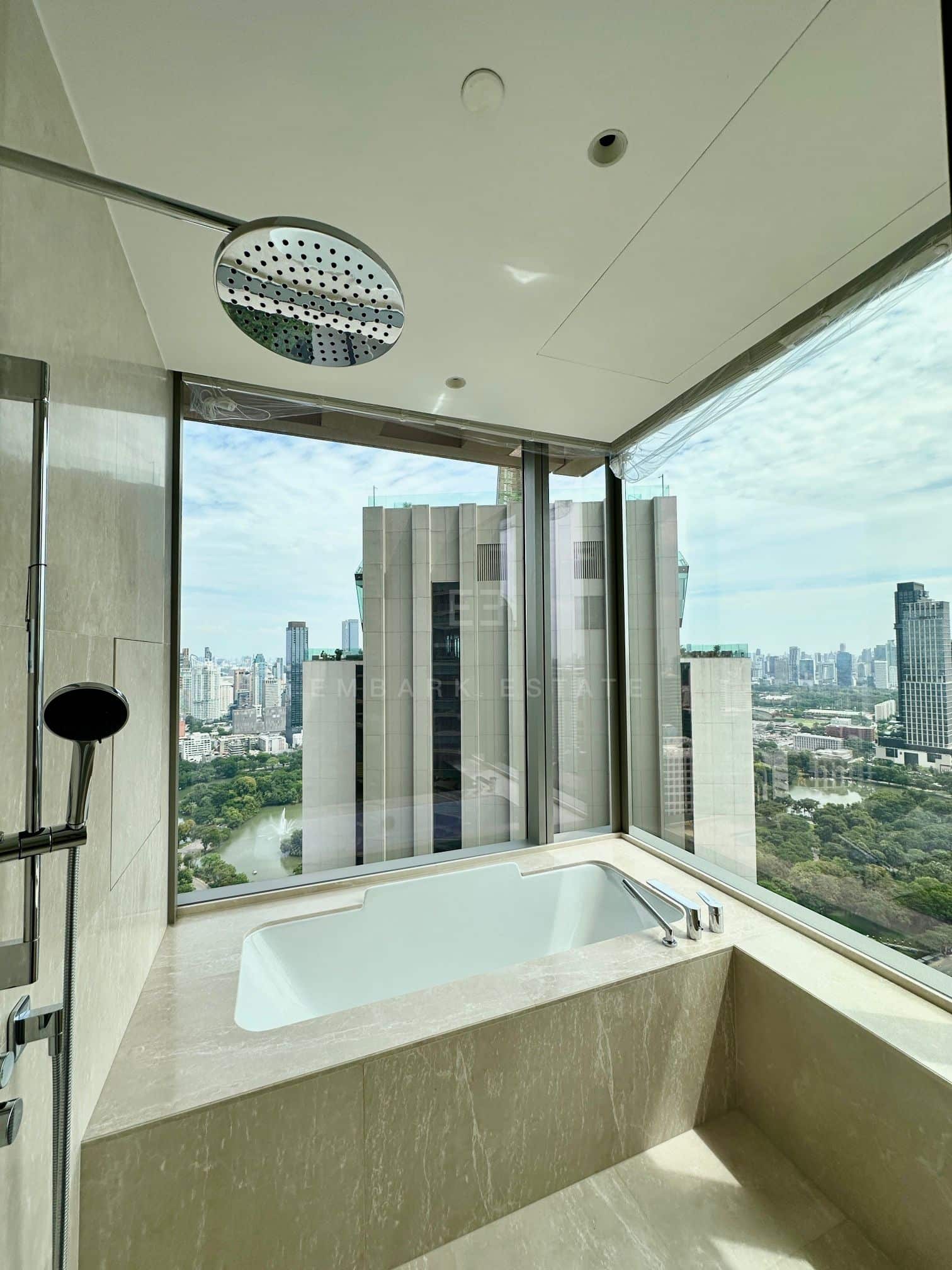 The principal bathroom of the residence at Dusit Residences, Dusit Central Park, a stone-set bathtub under a rain shower at the corner window, over the lake and fountain of Lumphini Park