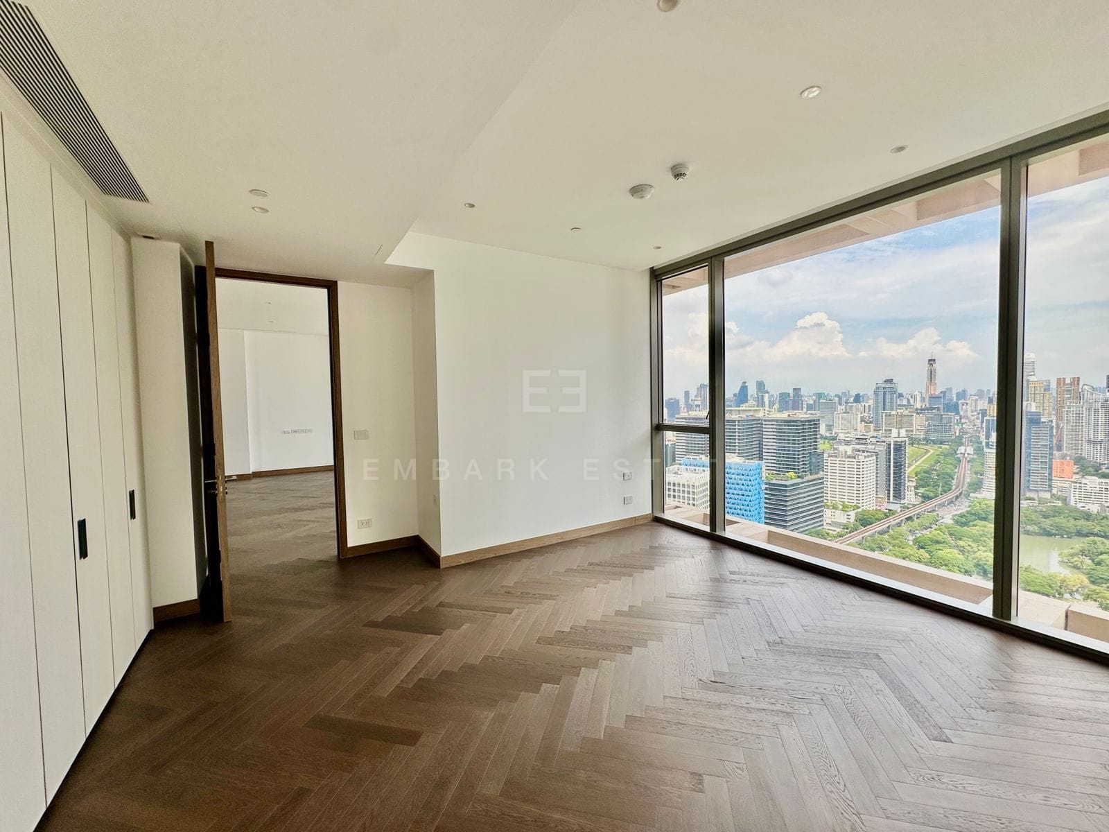 A bedroom of the residence at Dusit Residences, Dusit Central Park, a full-wall wardrobe and full-height glass over Lumphini Park, its lake and the skytrain line