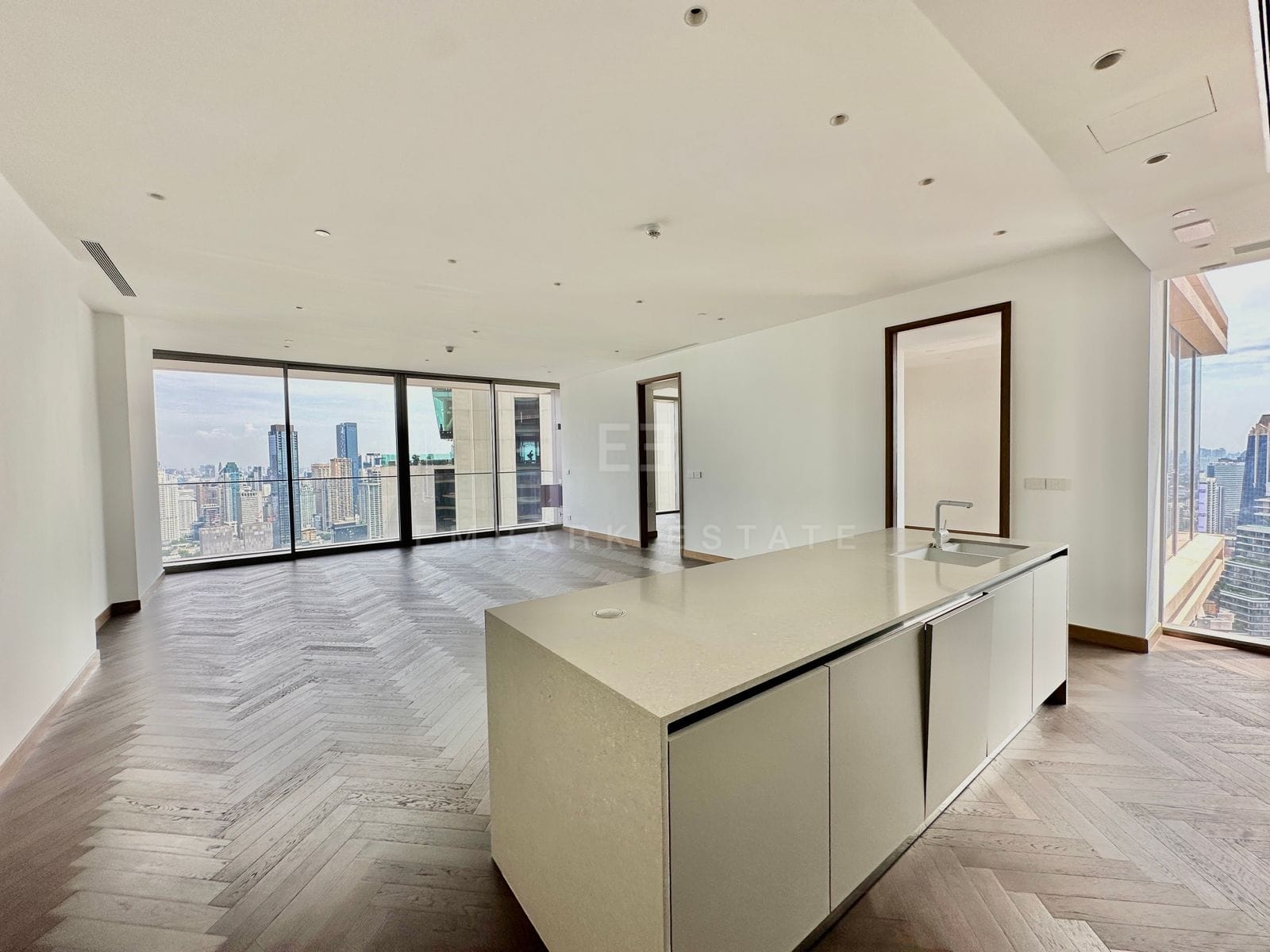 The open kitchen and living room of the residence at Dusit Residences, Dusit Central Park, the island in the foreground, the living room's glass wall and a corner window beyond