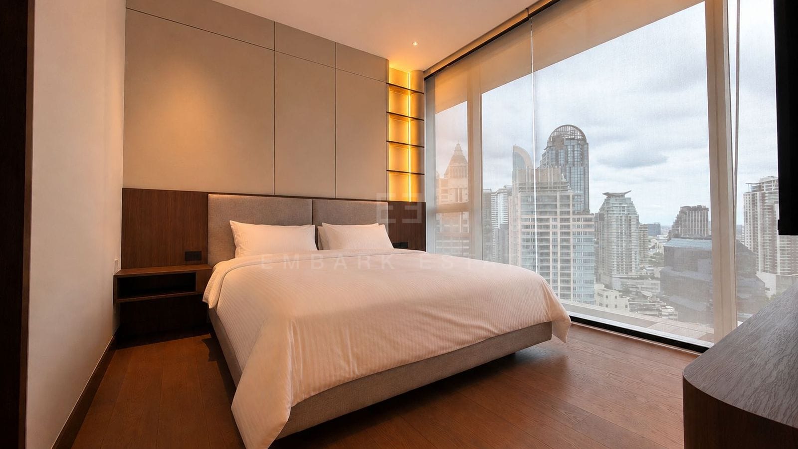 The bedroom of the 56 square metre residence at Dusit Parkside, Dusit Central Park, a timber-panelled headboard wall with a backlit niche beside full-height glazing over the city