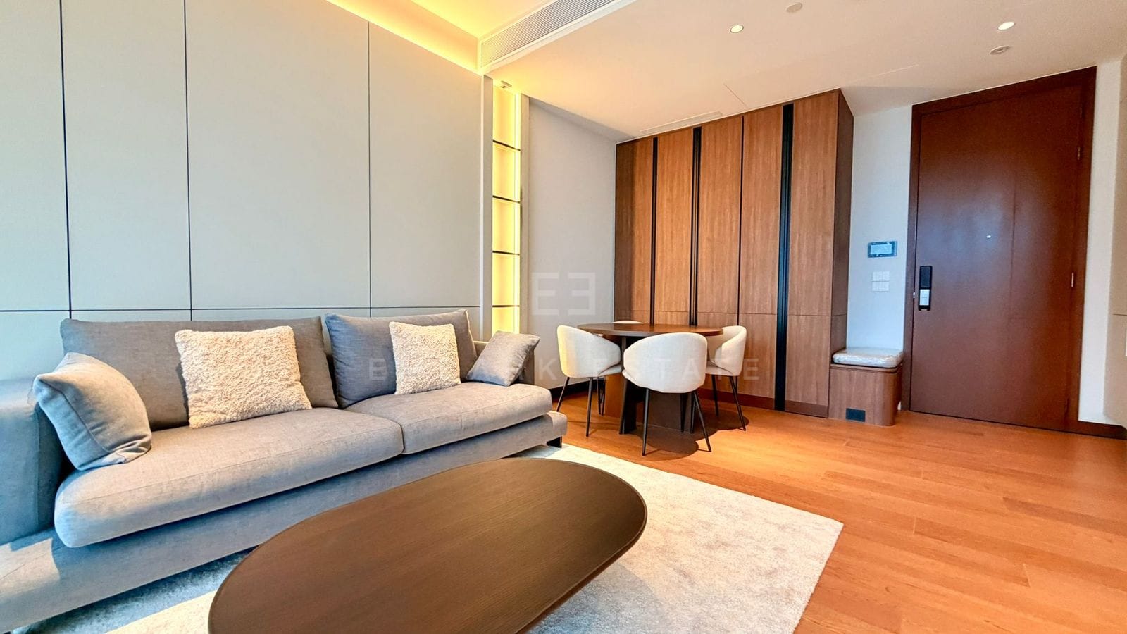 The living room at Dusit Parkside, Dusit Central Park, a sofa against a lit panelled wall with a timber table and a dining table for two