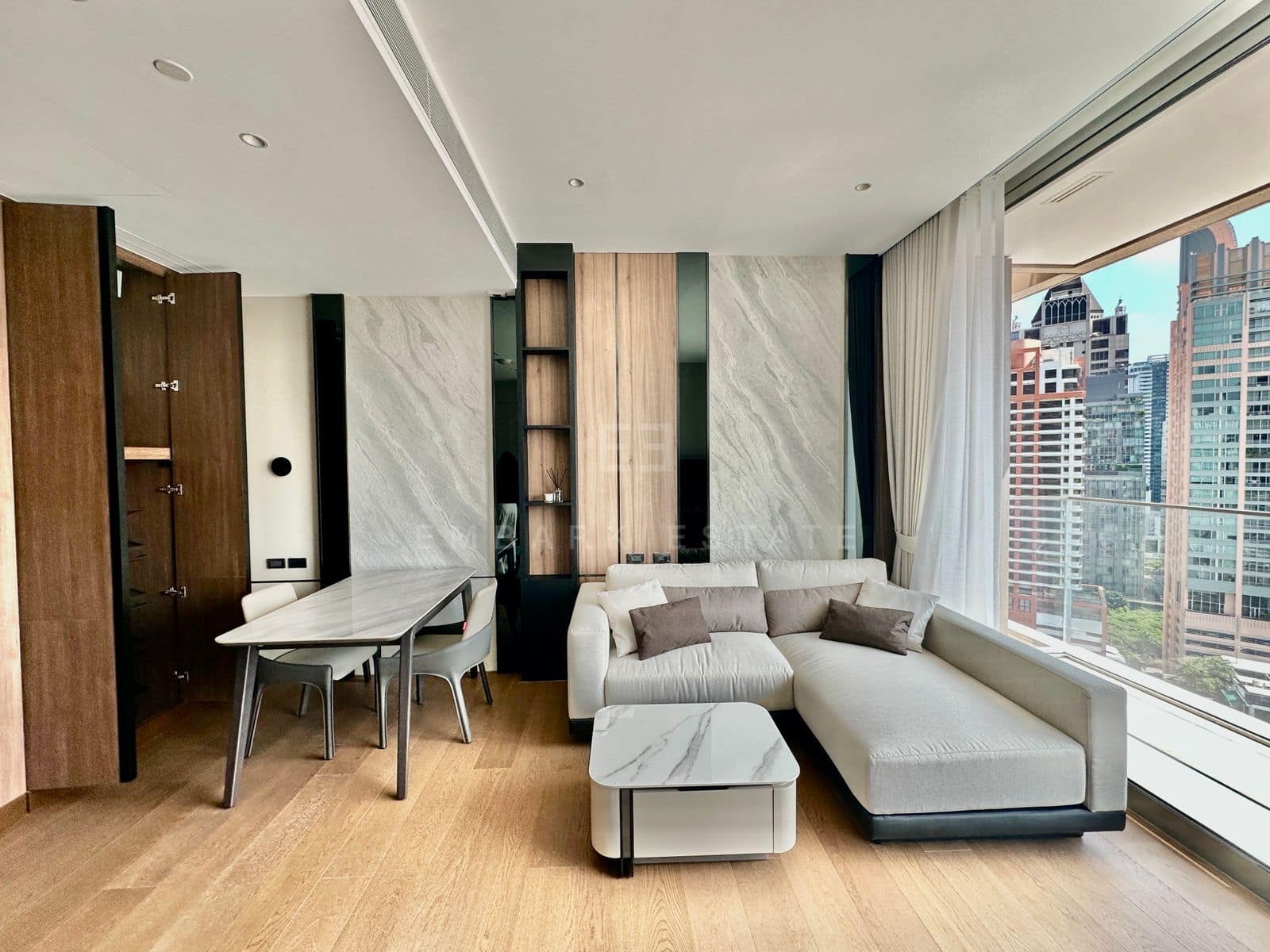 ห้องนั่งเล่นที่ Dusit Parkside, Dusit Central Park โต๊ะอาหารหินอ่อนข้างตู้ไม้วอลนัท และโซฟาเข้ามุมริมหน้าต่างที่มองเห็นอาคารสูงย่าน Silom