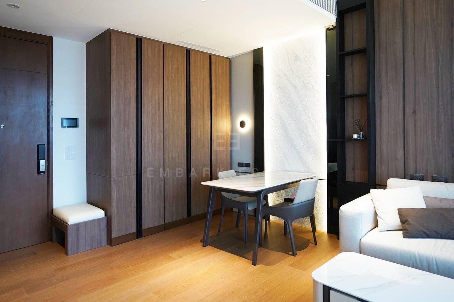 The entrance of the residence at Dusit Parkside, Dusit Central Park, a full-height walnut wardrobe wall and a bench beside the front door, the dining table against the lit stone wall