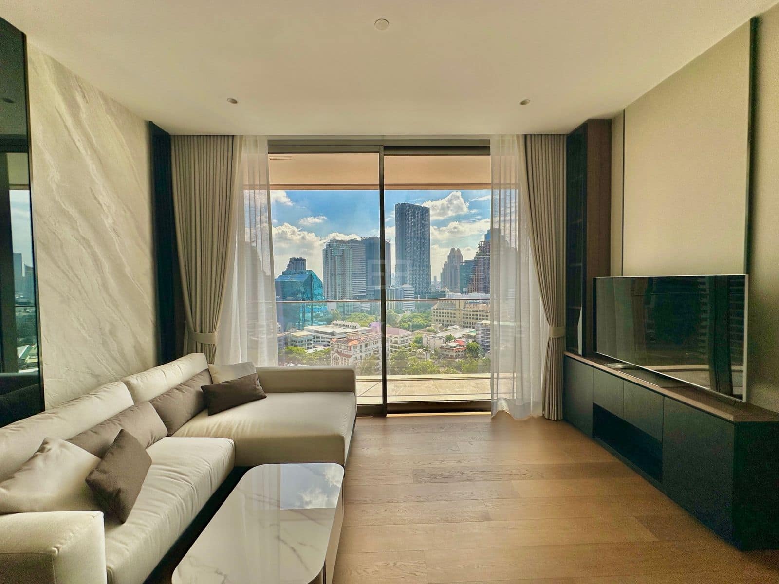 The living room at Dusit Parkside, Dusit Central Park, a cream sofa facing the television, sliding glass open onto the balcony and the central Bangkok skyline