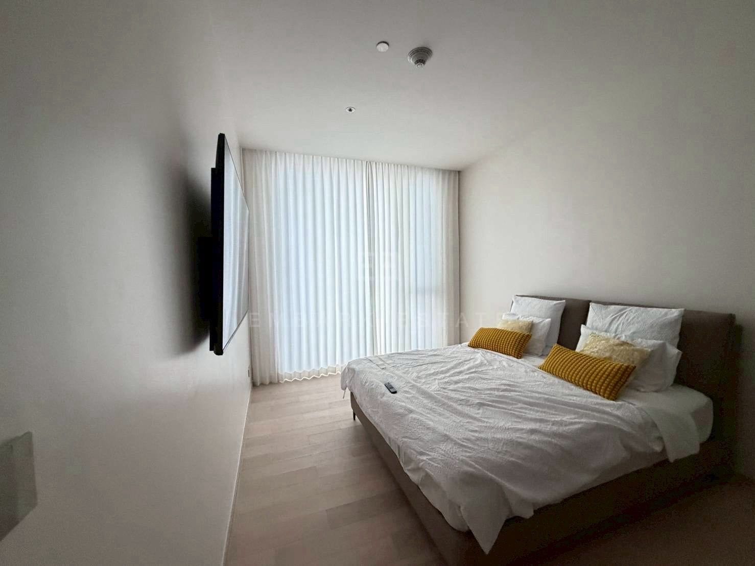 A bedroom at EI8HTEEN SEVEN, a taupe upholstered headboard with the television on the wall opposite