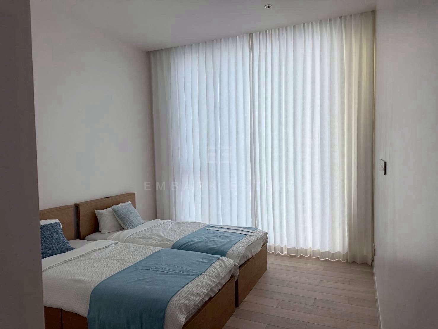 A bedroom at EI8HTEEN SEVEN, twin beds against a timber headboard with sheer curtains across the glazing