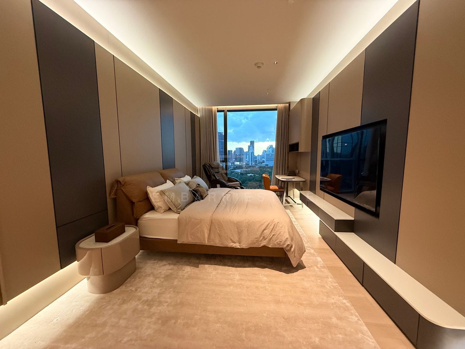 Principal bedroom at EI8HTEEN SEVEN, Bangkok, looking past the bed to a picture window over Lumphini Park, with a television set into the joinery wall