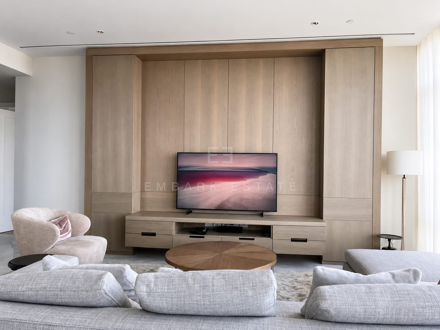 The living room at Four Seasons Private Residences, the television set into an oak panelled wall with curved armchairs and a round timber table