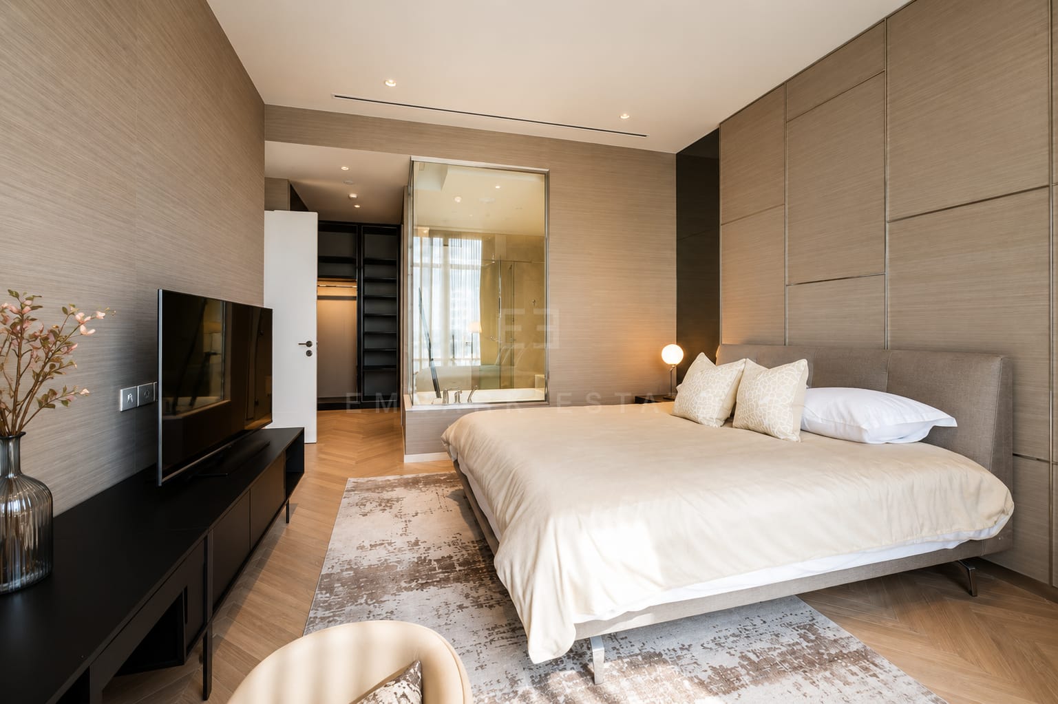 A bedroom at Four Seasons Private Residences, an oak panelled wall behind the television with the wardrobe and glazed bathroom through the door