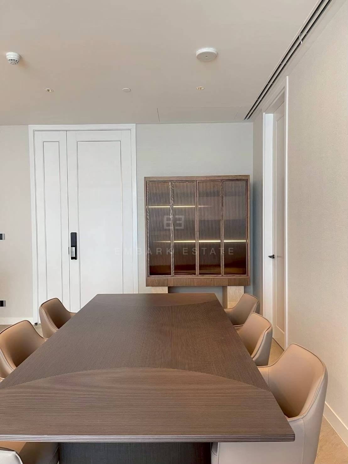 The dining table at ONE89 Wireless in walnut with cream leather chairs, a fluted-glass display cabinet on the wall behind