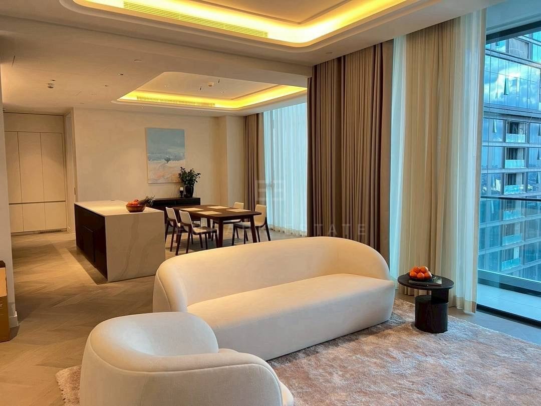 The living room of the 151 square metre residence at ONE89 Wireless, a curved sofa and armchair on a wool rug with the dining table and kitchen island beyond