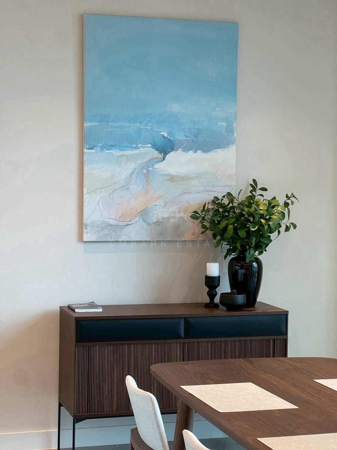 The dining area at ONE89 Wireless, a ribbed walnut sideboard beneath a blue abstract canvas beside the dining table