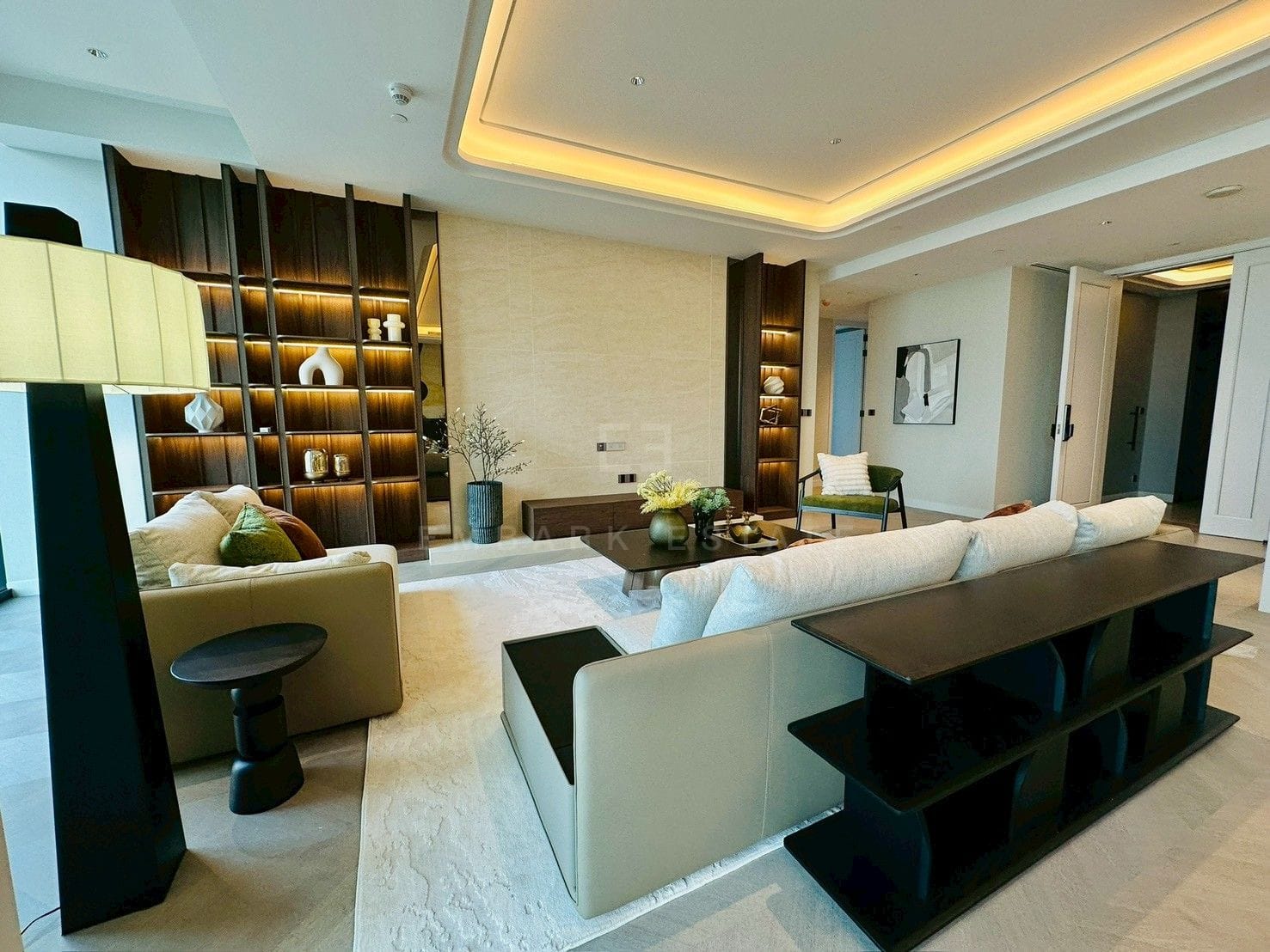 Living room at ONE89 Wireless, Bangkok, with lit dark-timber shelving either side of a travertine wall and a console behind the sofa