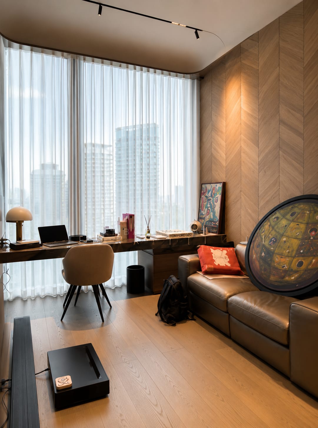 The study at Scope Langsuan, a long walnut desk at the window with a leather sofa against a herringbone panelled wall
