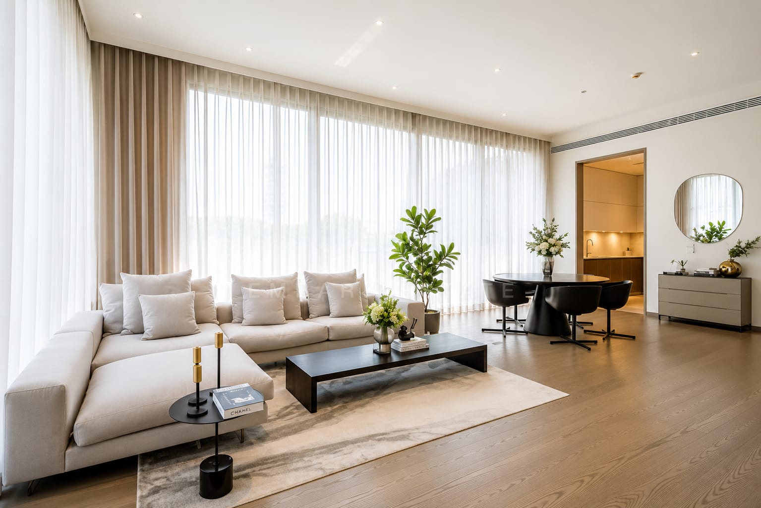 The living room of the 160 square metre residence at Scope Langsuan, a cream sectional on a rug with sheer curtains along the glazing and the dining table beyond