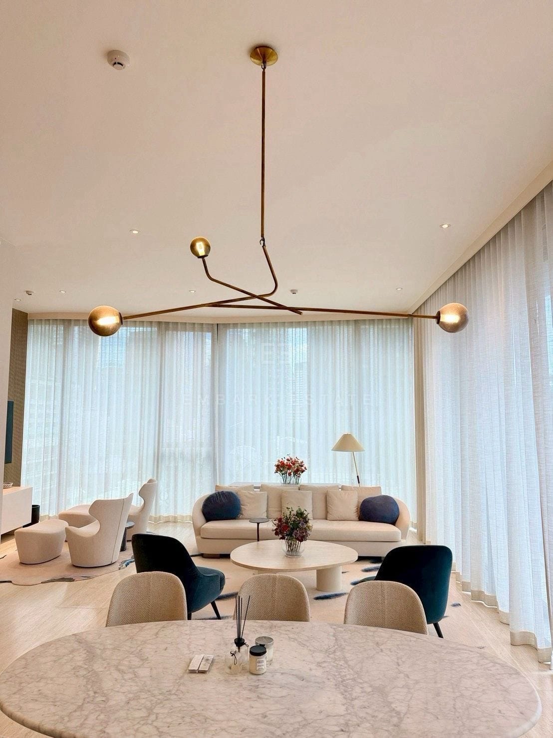Living room at Scope Langsuan, Bangkok, under a brass mobile chandelier, with the marble dining table in the foreground