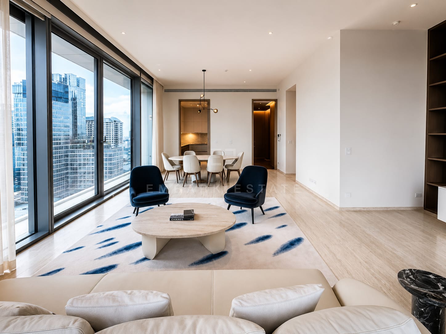 The living room at Scope Langsuan from the far end, the seating group on a blue-flecked rug with the dining table and kitchen beyond