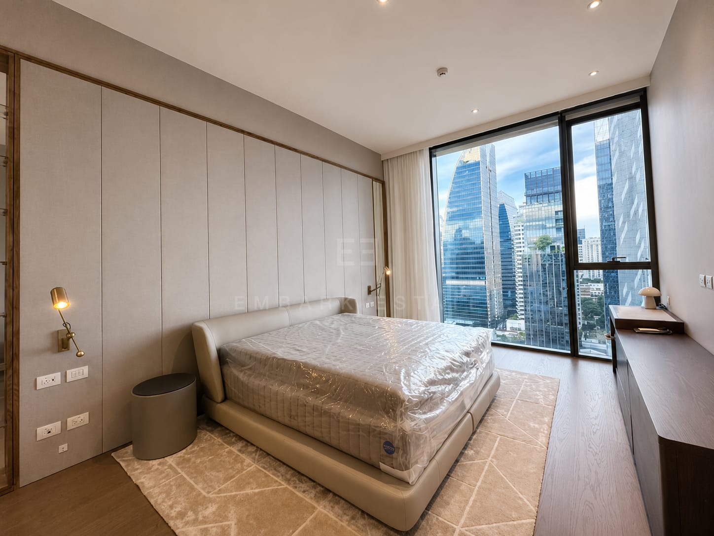 The main bedroom at Scope Langsuan, a fabric-panelled headboard wall with brass wall lights above a long timber console