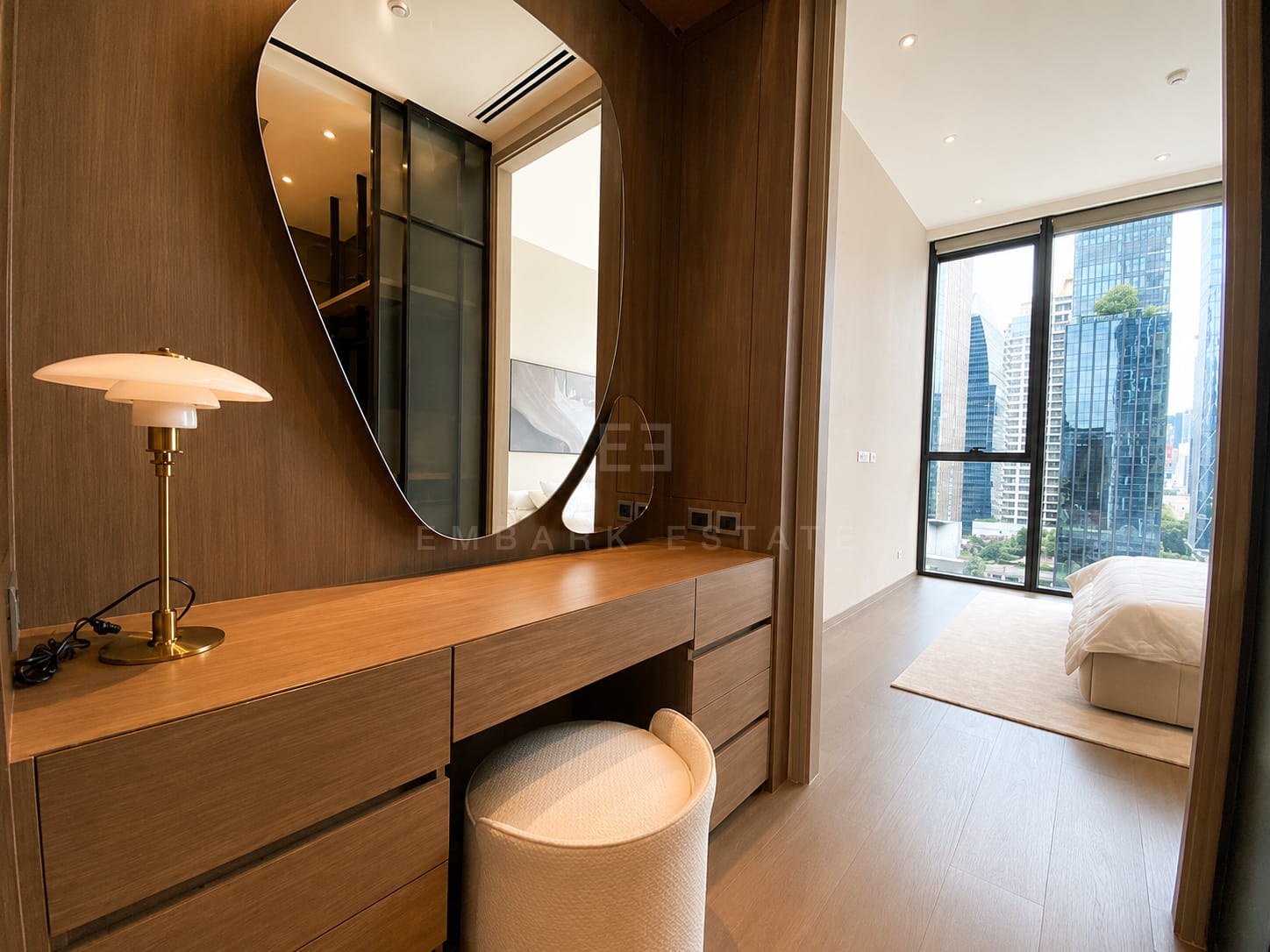 The dressing table at Scope Langsuan, an organic mirror on a timber wall above a long counter with a bouclé stool