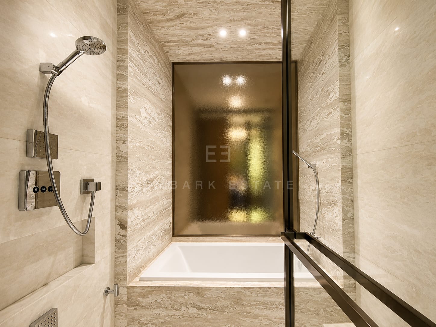 The bathroom at Scope Langsuan, a rain shower in travertine with the bath behind a fluted glass screen