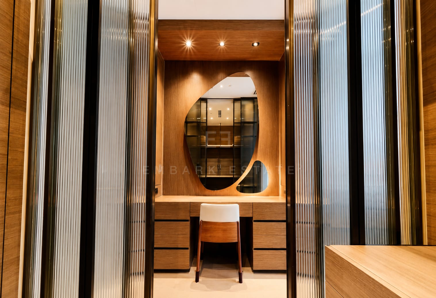 The dressing alcove at Scope Langsuan seen through the fluted glass doors, an organic mirror above a timber desk